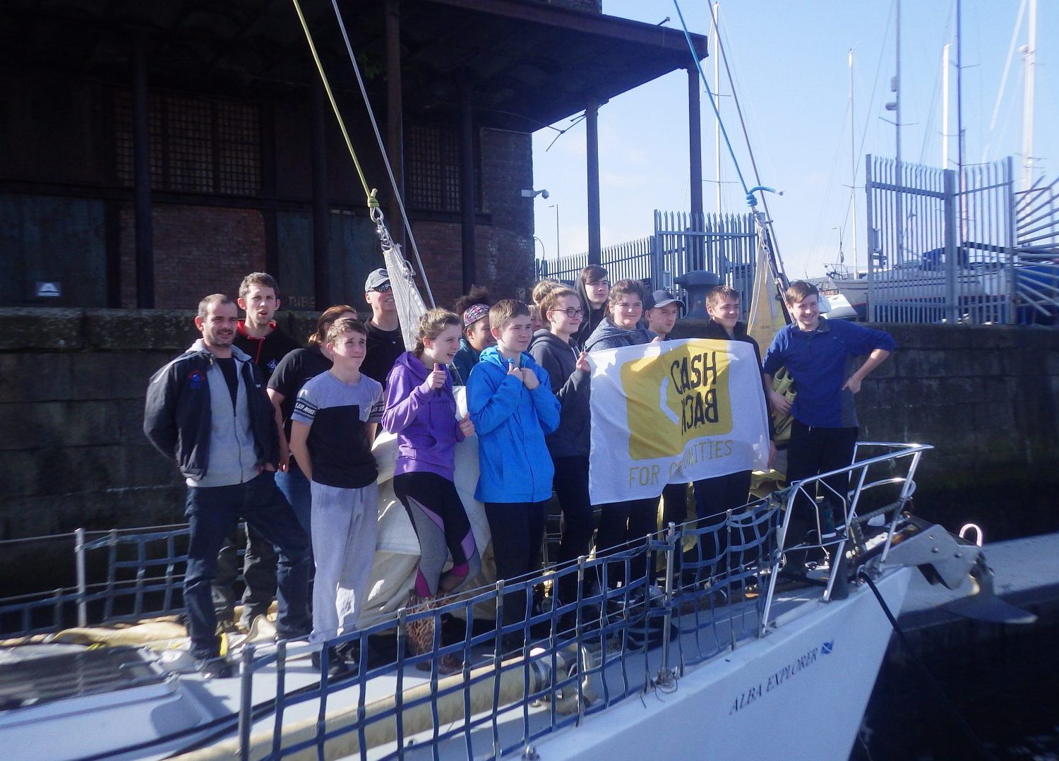 Group of young people, sea staff and volunteers aboard OYT Scotland vessel holding the Cashback for Communities