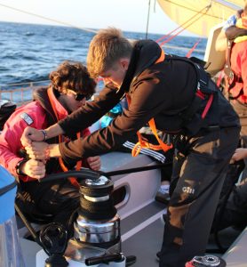 Two young people turn the winch aboard Alba Explorer, with the sun set upon them.