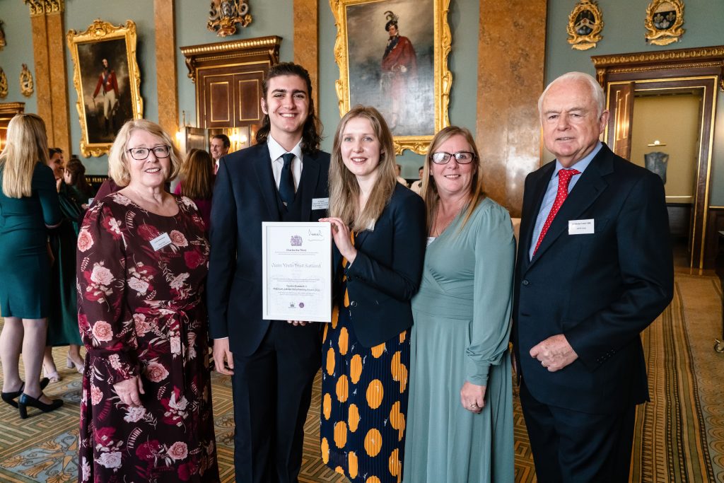 Chair and CEO of OYT Scotland stand with two young volunteers who hold the Queen Elizabeth II's Platinum Jubilee Volunteering Award. Standing with the group is Sir Martyn Lewis, Chair of the KAVS.