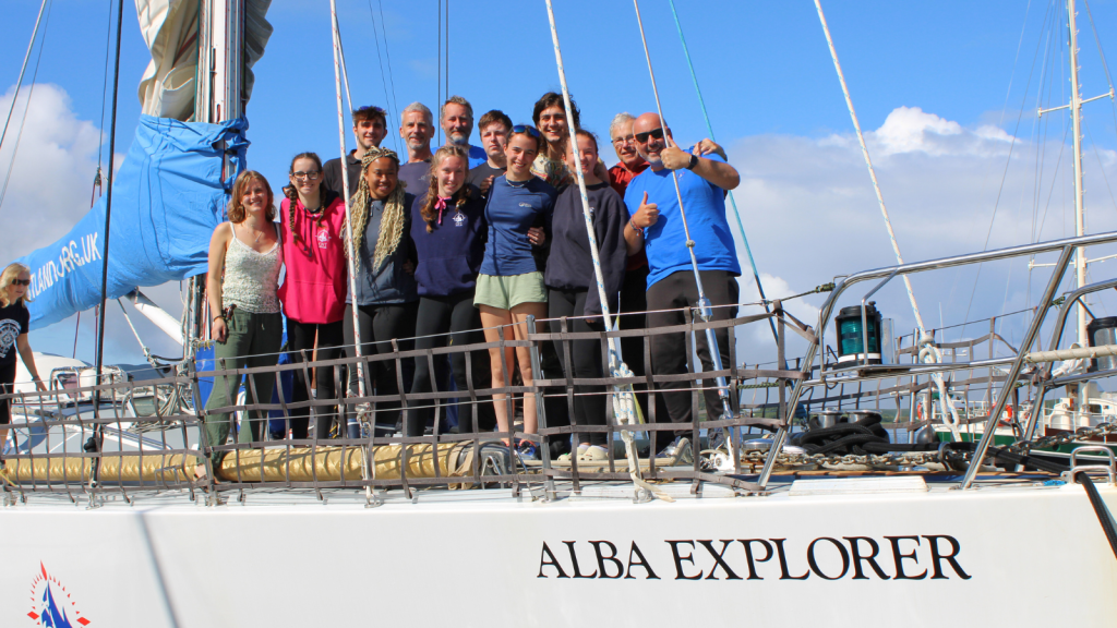 Paul stands with a crew aboard Alba Explorer. Young people stand at the front, and sea staff are standing behind them.